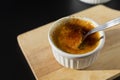 Homemade creme brulee in white ramekin  with sugar burn top up cracking with spoon on black background with copy space. French Royalty Free Stock Photo