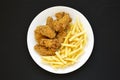 Homemade Crispy Chicken Wings and French Fries on a white plate on a black background, top view. From above, overhead, flat lay Royalty Free Stock Photo