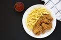 Homemade Crispy Chicken Wings and French Fries on a white plate on a black background, top view. From above, overhead, flat lay. Royalty Free Stock Photo