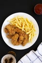 Homemade Crispy Chicken Wings and French Fries on a white plate on a black surface, top view. From above, overhead, flat lay Royalty Free Stock Photo