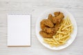 Homemade Crispy Chicken Wings and French Fries on a white plate, blank notepad on a white wooden background, top view Royalty Free Stock Photo