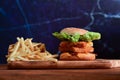 Homemade fish burger with cheese, lettuce, and fried potatoes on wooden table. Royalty Free Stock Photo