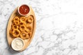 Homemade crunchy fried onion rings with sauces on marble table, top view