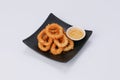 Homemade crunchy fried onion rings with sweet sauce in a black dish on white background. Royalty Free Stock Photo
