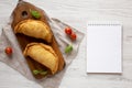 Homemade Deep Fried Italian Panzerotti Calzone on a rustic wooden board, blank notepad on a white wooden background, top view. Royalty Free Stock Photo