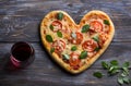 Homemade delicious margarita pizza with tomatoes and basil in the shape of a heart with a glass of red wine on a wooden table for Royalty Free Stock Photo