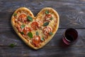 Homemade delicious margarita pizza with tomatoes and basil in the shape of a heart with a glass of red wine on a wooden table for Royalty Free Stock Photo