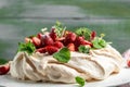 Homemade delicious meringue cake Pavlova with whipped cream, fresh strawberrie and mint on wooden background, close up view