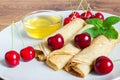 Homemade dessert. Fried pancakes with honey. Crepe with black cherry on white plate background.