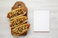 Homemade detroit style chili dog on a rustic wooden board, blank notepad on a white wooden background, top view. Copy space Royalty Free Stock Photo