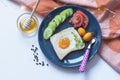 Homemade egg in a hole with toast bread and vegetables on a blue ceramic plate with black peppercorns on a white table with lights Royalty Free Stock Photo