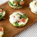 Homemade Egg White Breakfast Cups with Spinach and Tomato on a rustic wooden board, side view. Close-up