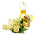 Homemade elderberry flower syrup in a bottle and lemonade drink in a glass, lemon zest and some fresh blossoms against a white