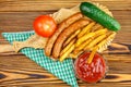 Homemade fast food, portion of french fries, ketchup, grilled sausages, tomato, cucumber on wooden board. Royalty Free Stock Photo