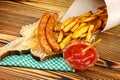 Homemade fast food, portion of french fries, ketchup, grilled sausages, on wooden board. Royalty Free Stock Photo