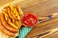 Homemade fast food, portion of french fries, ketchup, grilled sausages, on wooden board. Royalty Free Stock Photo