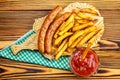 Homemade fast food, portion of french fries, ketchup, grilled sausages on wooden board.