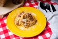 Homemade Fettuccine pasta with minced meat and sprinkled with shredded cheese. Hot portion of a dish on yellow plate on a table co