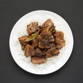 Homemade Filipino Adobo Pork with rice on a white plate on a black surface, top view. Asian food. Flat lay, overhead, from above