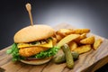 homemade fish burger with cheese, vegetables, and tartar sauce on a wooden cutting board.