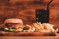 Fish burger with fried potatoes and glass of soft drink on wooden table. Royalty Free Stock Photo