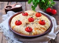 Homemade focaccia with cherry tomatoes, sea salt and herbs in a clay bowl on a gray wooden background.