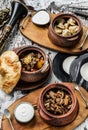 Homemade food, fried dumplings, baked potatoes with meat, baked mushrooms with onions in clay pot with sour cream on wooden board