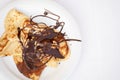 Homemade, freshly prepared pancakes drenched in chocolate on a white plate on a table with a white tablecloth. Place for your text