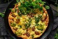 Homemade Frittata with mushrooms, broccoli, feta cheese, green peas and bacon on black plate
