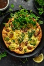 Homemade Frittata with mushrooms, broccoli, feta cheese, green peas and bacon on black plate