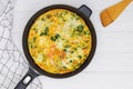 Homemade frittata or omelette with mix of vegetables in iron skillet on white table,