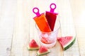 Homemade frozen popsicles made with watermelon on ice in glass on wooden background