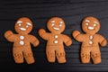 Homemade gingerbread cookies covered with icing, three gingerbread men waving hand and smiling, on black wooden background Royalty Free Stock Photo