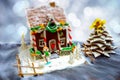 Homemade gingerbread house, gingerbread Christmas tree and a sugar mastic snowman on background of defocused silver lights