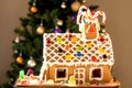 Homemade gingerbread house decorated with icing, sweets , lollies and candy canes with blurred Christmas tree on background Royalty Free Stock Photo