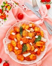 Homemade gnocchi served with tomato, basil, parmesan cheese in a white antique plate on a pastel tablecloth with cutlery.