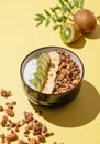 Homemade granola or muesli with banana, kiwi, nuts and yogurt in a bowl on a yellow background with fresh fruits