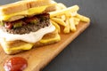 Homemade Grilled Cheese Burger with French Fries on a rustic wooden board on a black surface, low angle view. Close-up Royalty Free Stock Photo