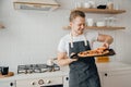 Homemade Italian pizza, handsome young male chef in dark apron holds baking sheet in bright kitchen. Cooking video blog Royalty Free Stock Photo