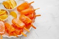 Homemade, juicy, orange popsicles. Placed on a white plate with ice cubes