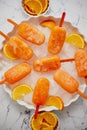 Homemade, juicy, orange popsicles. Placed on a white plate with ice cubes