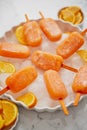 Homemade, juicy, orange popsicles. Placed on a white plate with ice cubes