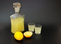 Homemade lemon liqueur, glass decanter and two glasses of drink and ripe citrus pieces on a black background Royalty Free Stock Photo