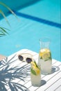 Homemade lemonade in glasses with lemon slice, on white table,in the edge of the pool with turquoise blue water Royalty Free Stock Photo