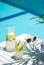 Homemade lemonade in glasses with lemon slice, on white table,in the edge of the pool with turquoise blue water Royalty Free Stock Photo