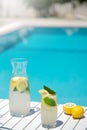 Homemade lemonade in glasses with lemon slice, on white table,in the edge of the pool with turquoise blue water Royalty Free Stock Photo