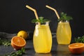 Homemade lemonade of lemons and oranges, decorated with mint in tall glasses with tubes on dark background, Horizontal format