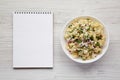 Homemade Macaroni Salad in a white bowl, blank notepad on a white wooden background, top view. Flat lay, overhead, from above. Royalty Free Stock Photo