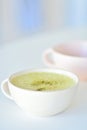 Homemade matcha latte on a white table, a light pink cup on the background, matcha green tea latte in a white cup with copy space Royalty Free Stock Photo