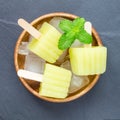 Homemade melon popsicles on grey slate, top view, square